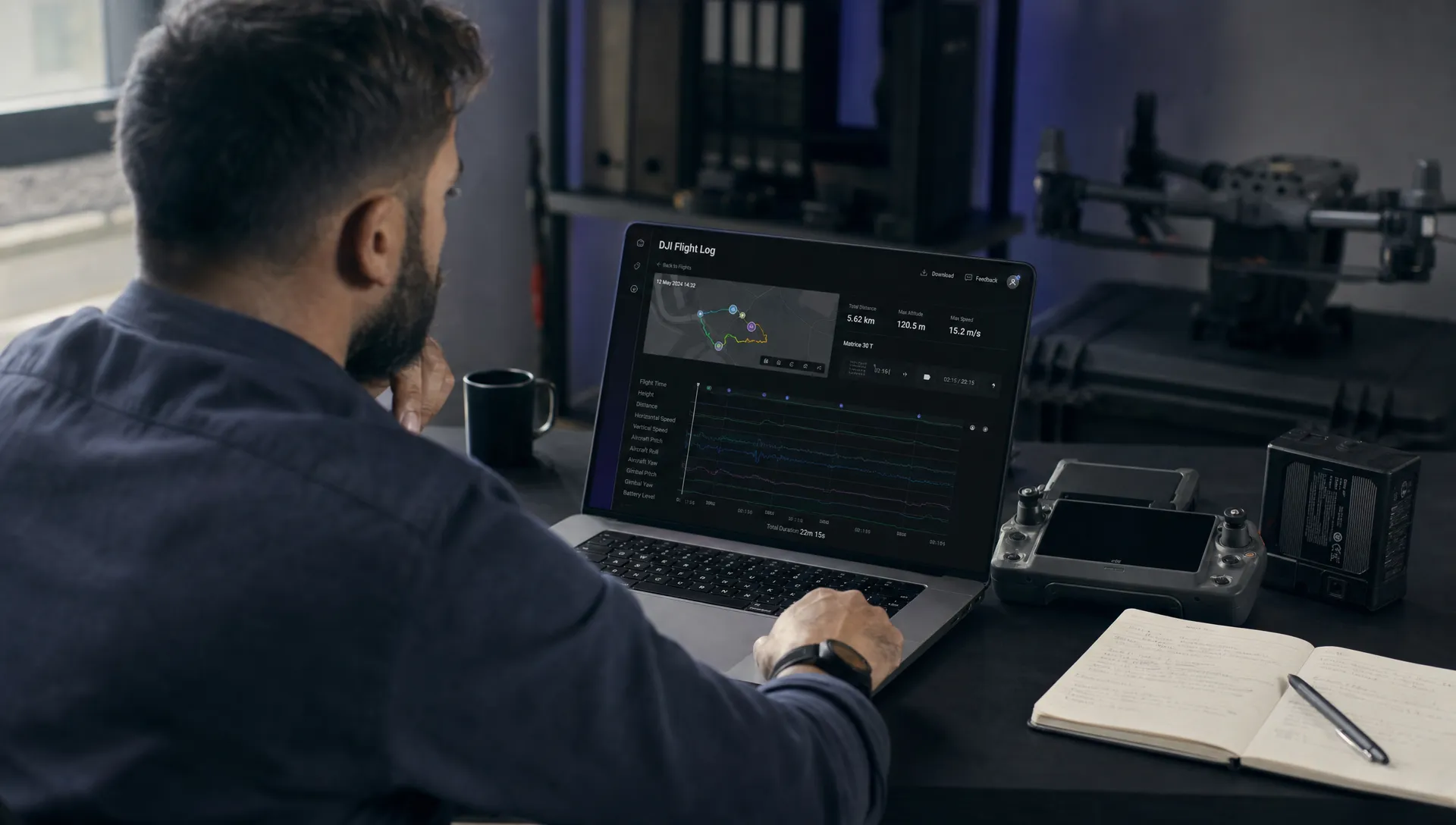 A drone operations manager reviews a DJI flight log timeline on a laptop with a controller, notebook and battery beside it.